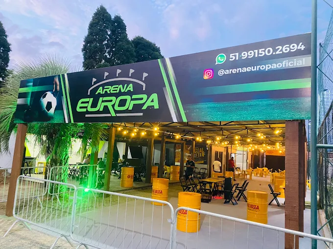 Área de bar da Arena Europa à noite, com mesas iluminadas ao lado do campo